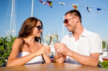love, dating, people and holidays concept - smiling couple wearing sunglasses drinking champagne and looking to each other at cafe