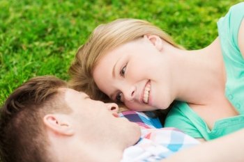 holidays, vacation, love and friendship concept - smiling couple lying on on grass in park