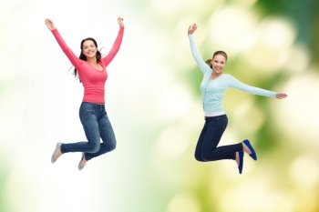 happiness, freedom, ecology, friendship and people concept - smiling young women jumping in air over green background