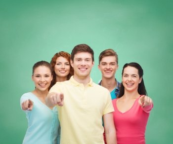 friendship, education, school and people concept - group of smiling teenagers pointing finger on you over green board background