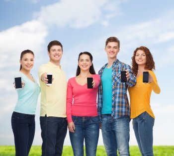 friendship, technology, summer and people concept - group of smiling teenagers with smartphones over blue sky and grass background