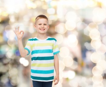 childhood, gesture, holidays and people concept - smiling little boy in casual clothes making OK gesture over sparkling background