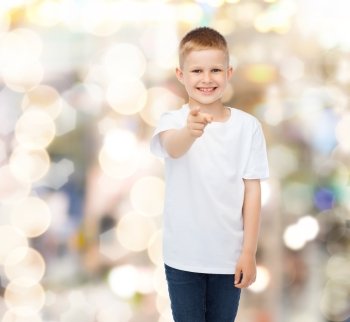 advertising, gesture, people and childhood concept - smiling boy in white blank t-shirt pointing finger at you over holidays background
