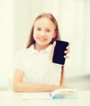 education, school, technology and internet concept - little student girl with notebook and black blank smartphone screen at school