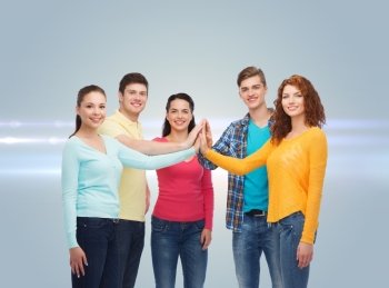 friendship, teamwork, gesture and people concept - group of smiling teenagers making high five over gray background with laser light