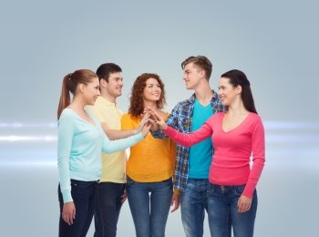 friendship, teamwork, gesture and people concept - group of smiling teenagers making high five over gray background with laser light