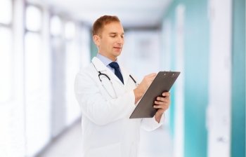 medicine, profession and healthcare concept - smiling male doctor with clipboard and stethoscope writing prescription over hospital background