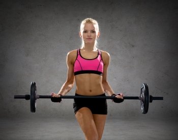 fitness, sport and dieting concept - sporty woman exercising with barbell over concrete wall background