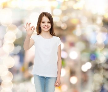 advertising, childhood, gesture, holidays and people - smiling little girl in white blank t-shirt showing ok sign over sparkling background