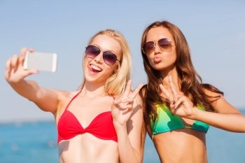 summer vacation, holidays, travel, technology and people concept - two smiling young women on beach making selfie with smartphone over blue sky background