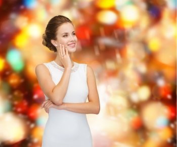 holidays, celebration, wedding and people concept - smiling woman in white dress wearing diamond ring over golden lights background