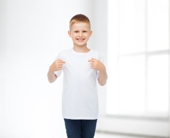 advertising, people, gesture and childhood concept - smiling boy in white blank t-shirt pointing finger himself over white room background