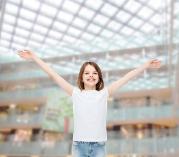 advertising, childhood, gesture, consumerism and people - smiling little girl in white blank t-shirt with stretched out arms over shopping center background