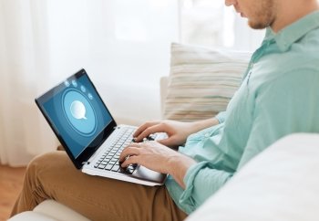 technology, leisure, advertisement and lifestyle concept - close up of man working with laptop computer displaying text bubble icon on screen and sitting on sofa at home