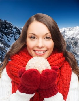 happiness, winter holidays and people concept - smiling young woman in red scarf and mittens with christmas ball over blue snowy background