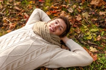 season, happiness and people concept - close up of smiling young man lying on ground or grass and fallen leaves in autumn park