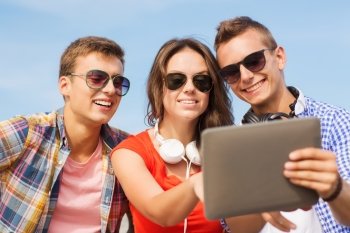 friendship, leisure, summer, technology and people concept - group of smiling friends with tablet pc computer and headphones sitting outdoors
