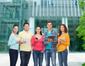 friendship, technology, education, business and people concept - group of smiling teenagers with smartphones and tablet pc computers over campus background