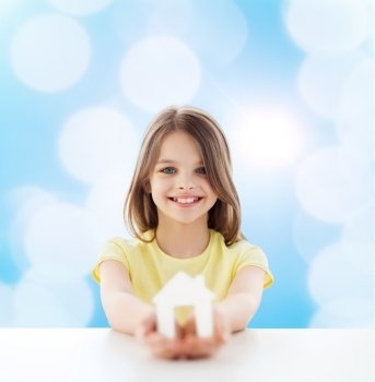 home, education, happiness, childhood and people concept - beautiful little girl sitting at table holding white house cutout over blue background