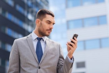 business, technology and people concept - serious businessman with smartphone over office building