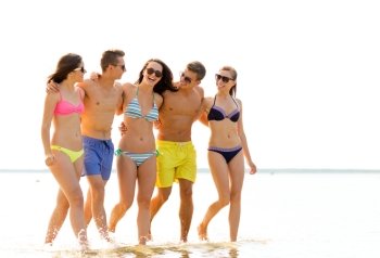friendship, sea, summer vacation, holidays and people concept - group of smiling friends wearing swimwear and sunglasses walking on beach