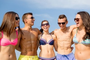 friendship, sea, summer vacation, holidays and people concept - group of smiling friends wearing swimwear and sunglasses talking on beach