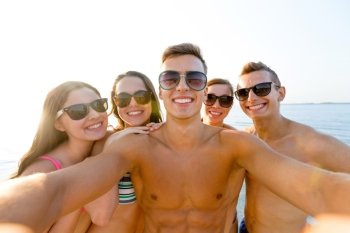 friendship, leisure, summer, technology and people concept - group of smiling friends making selfie on beach