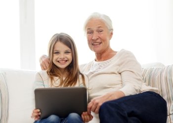 family, generation, technology and people concept - smiling granddaughter and grandmother with tablet pc computer sitting on couch at home