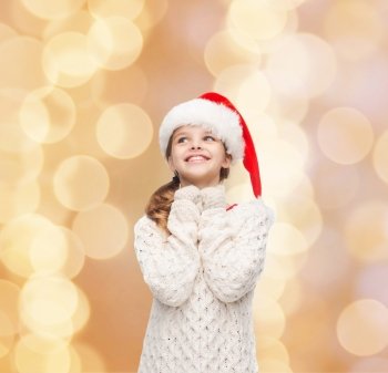 christmas, holidays, childhood and people concept - smiling girl in santa helper hat over beige lights background