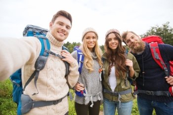 adventure, travel, tourism, hike and people concept - group of smiling friends with backpacks making selfie outdoors