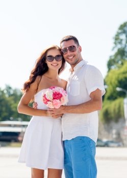 love, wedding, summer, dating and people concept - smiling couple wearing sunglasses standing with bunch of flowers in city