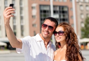 love, wedding, summer, dating and people concept - smiling couple wearing sunglasses making selfie with smartphone in city