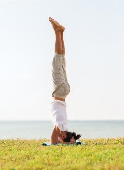 fitness, sport, people and lifestyle concept - man making yoga exercises on sand outdoors