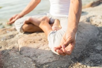 fitness, sport, people and lifestyle concept - close up of man making yoga exercises on pier outdoors