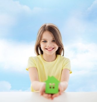 home, education, happiness, childhood and people concept - beautiful little girl sitting at table holding white house cutout over cloudy sky background