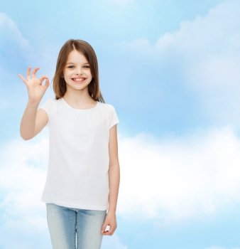 advertising, dream, gesture, childhood and people - smiling little girl in white blank t-shirt showing ok sign over cloudy sky background