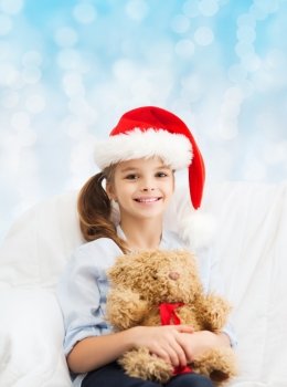 holidays, presents, christmas, childhood and people concept - smiling little girl with teddy bear toy over blue lights background