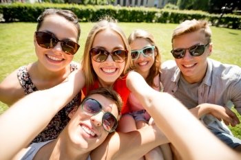 friendship, leisure, summer, technology and people concept - group of smiling friends making selfie with smartphone, camera or tablet pc in park