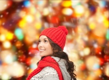 happiness, winter holidays, christmas and people concept - smiling young woman in red hat and scarf over red lights background