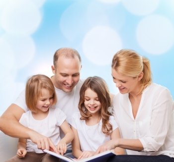 family, childhood, holidays and people - smiling mother, father and little girls reading book over blue lights background