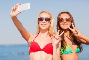 summer vacation, holidays, travel, technology and people concept - two smiling young women on beach making selfie with smartphone over blue sky background