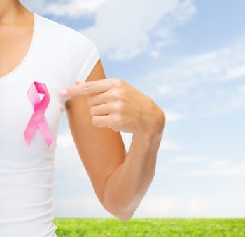 healthcare, people, charity and medicine concept - close up of woman in t-shirt with pink breast cancer awareness ribbon over blue sky and grass background