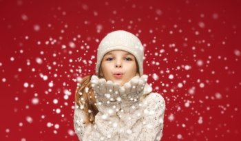 christmas, xmas and happiness concept - happy girl in winter clothes blowing on palms