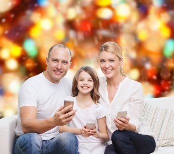 family, holidays, technology and people concept - smiling mother, father and little girl with smartphones over red lights background