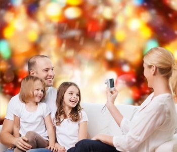 family, holidays, technology and people - smiling mother, father and little girls with camera over red lights background
