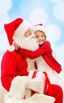 holidays, christmas, childhood and people concept - smiling little girl hugging with santa claus over blue lights background