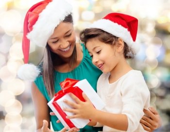 christmas, holidays, celebration, family and people concept - happy mother and little girl in santa helper hats with gift box over lights background