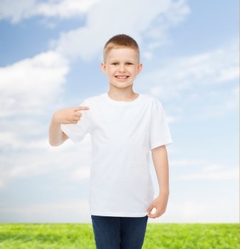 advertising, people and childhood concept - smiling little boy in white blank t-shirt pointing finger at himself over natural background