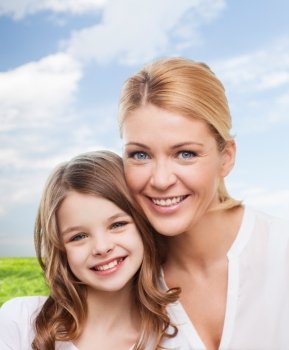 family, childhood, happiness and people - smiling mother and little girl over blue sky and grass background