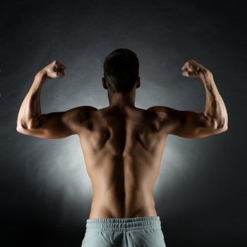 sport, bodybuilding, strength and people concept - young man showing biceps over gray background from back